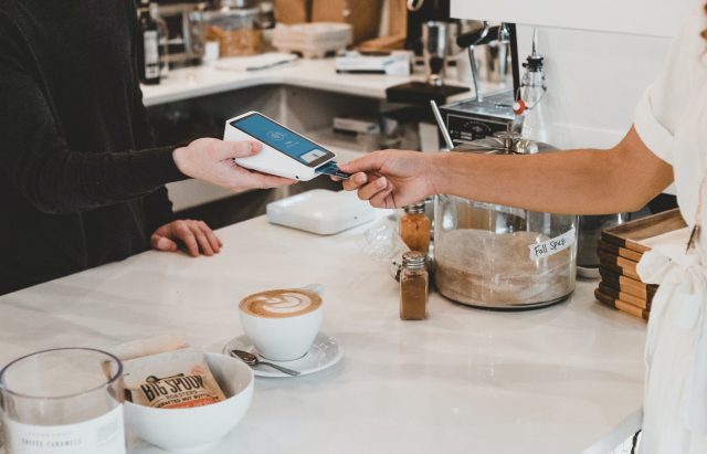 Frau bezahlt im Café mit Karte an einem mobilen Bezahlsystem.
